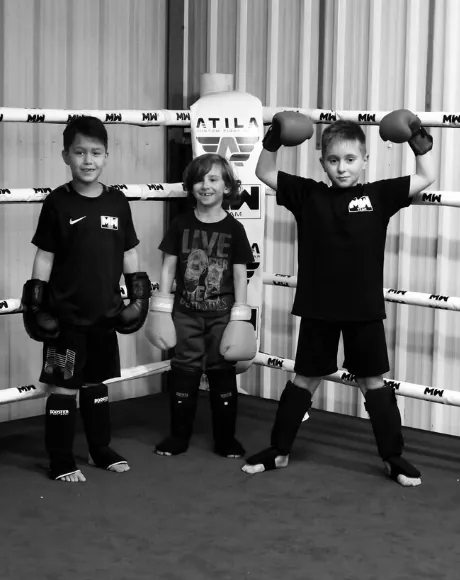 Drie kinderen met bokshandschoenen en scheenbeschermers in de ring